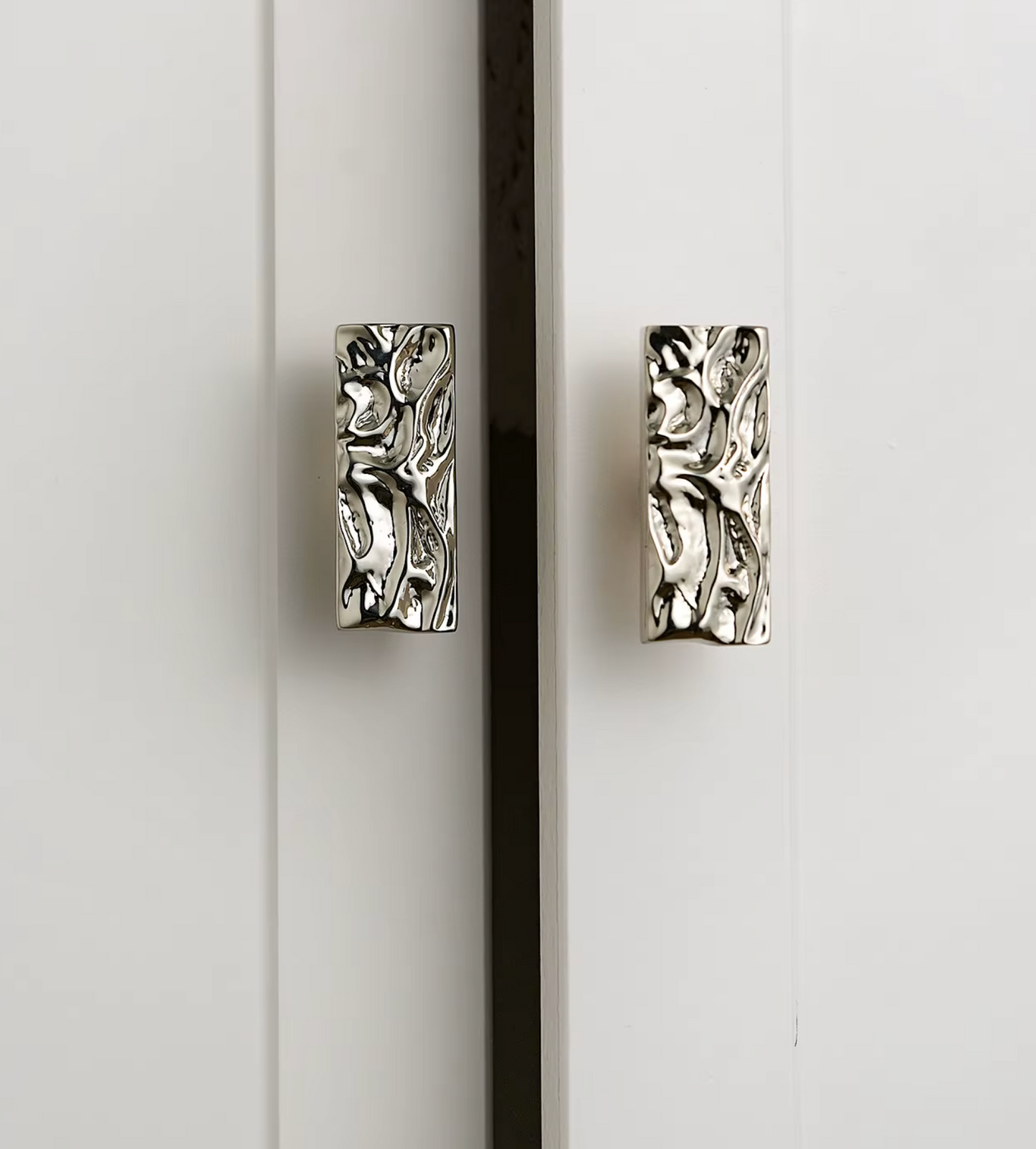 Two rectangular silver cabinet pulls with an embossed textured, organic pattern, mounted on white paneled doors.