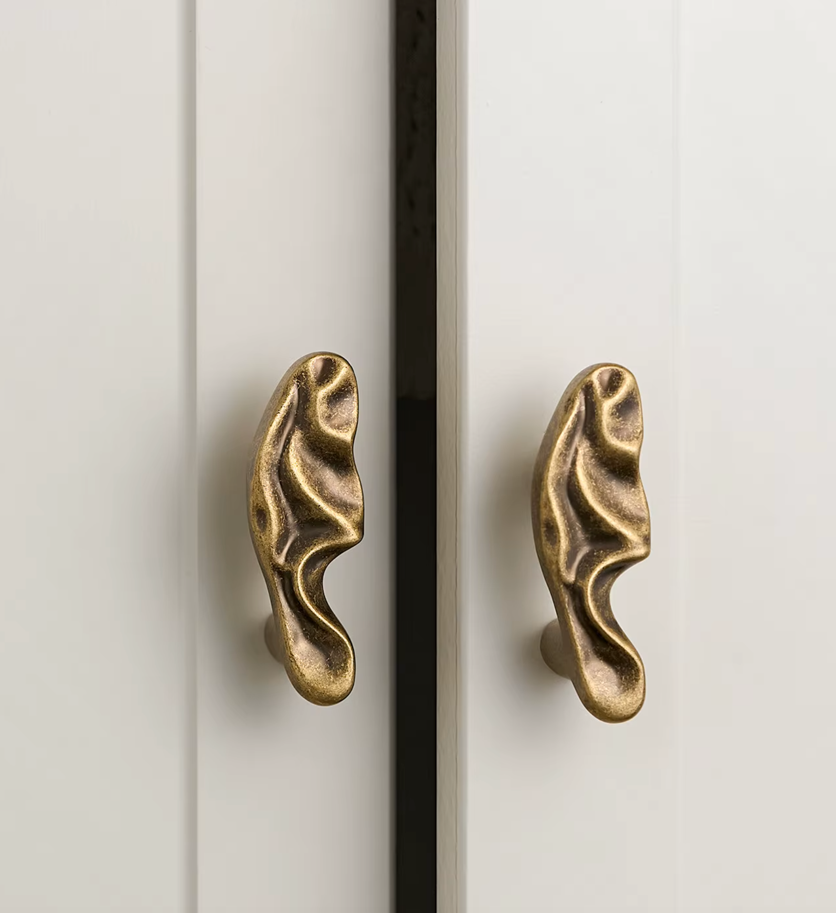 Two sculptural cabinet pulls shaped like stylized ears in an antique brass finish, mounted on white paneled doors.