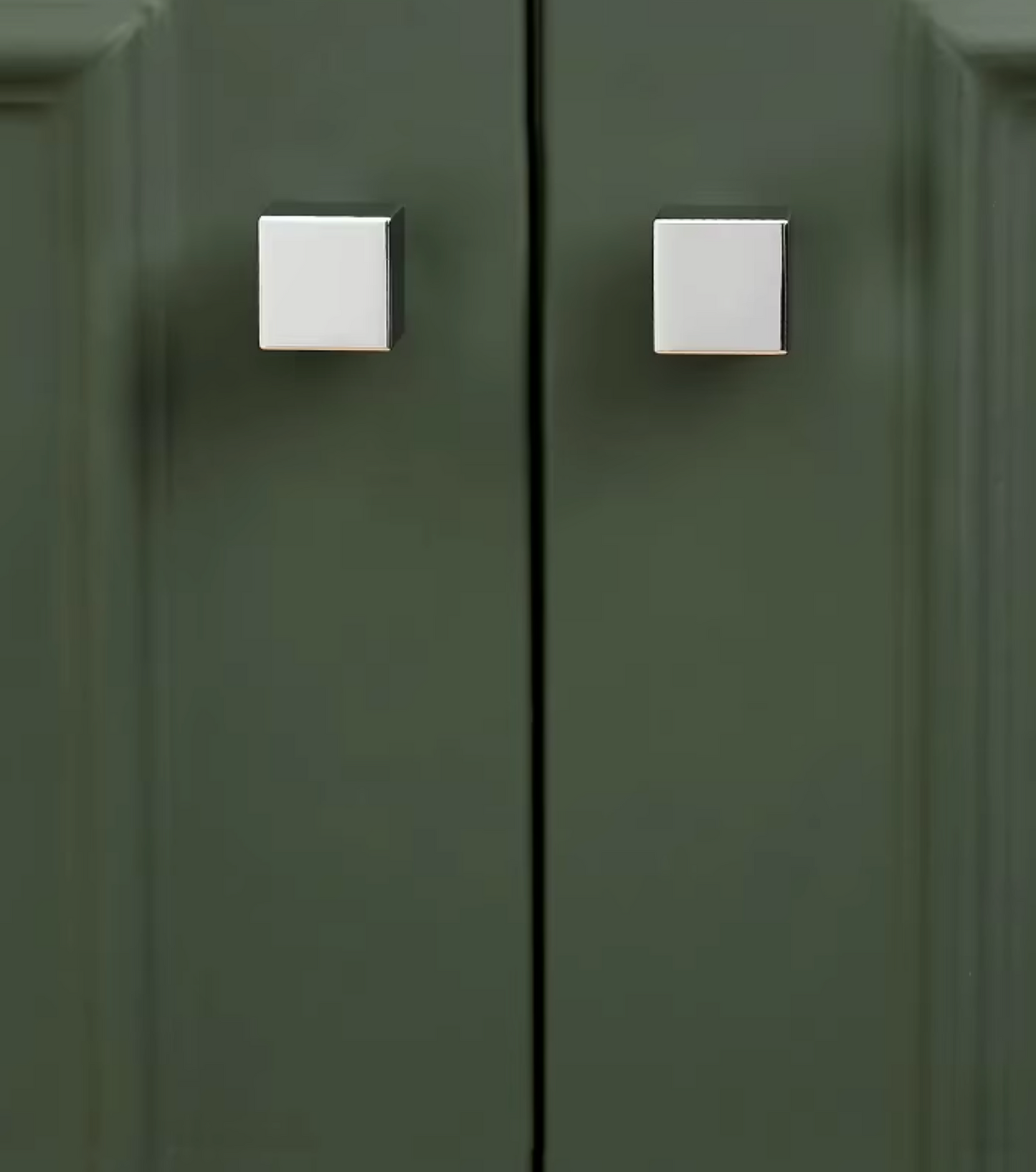 A close-up of a dark olive green cabinet door with two square silver metal knobs.