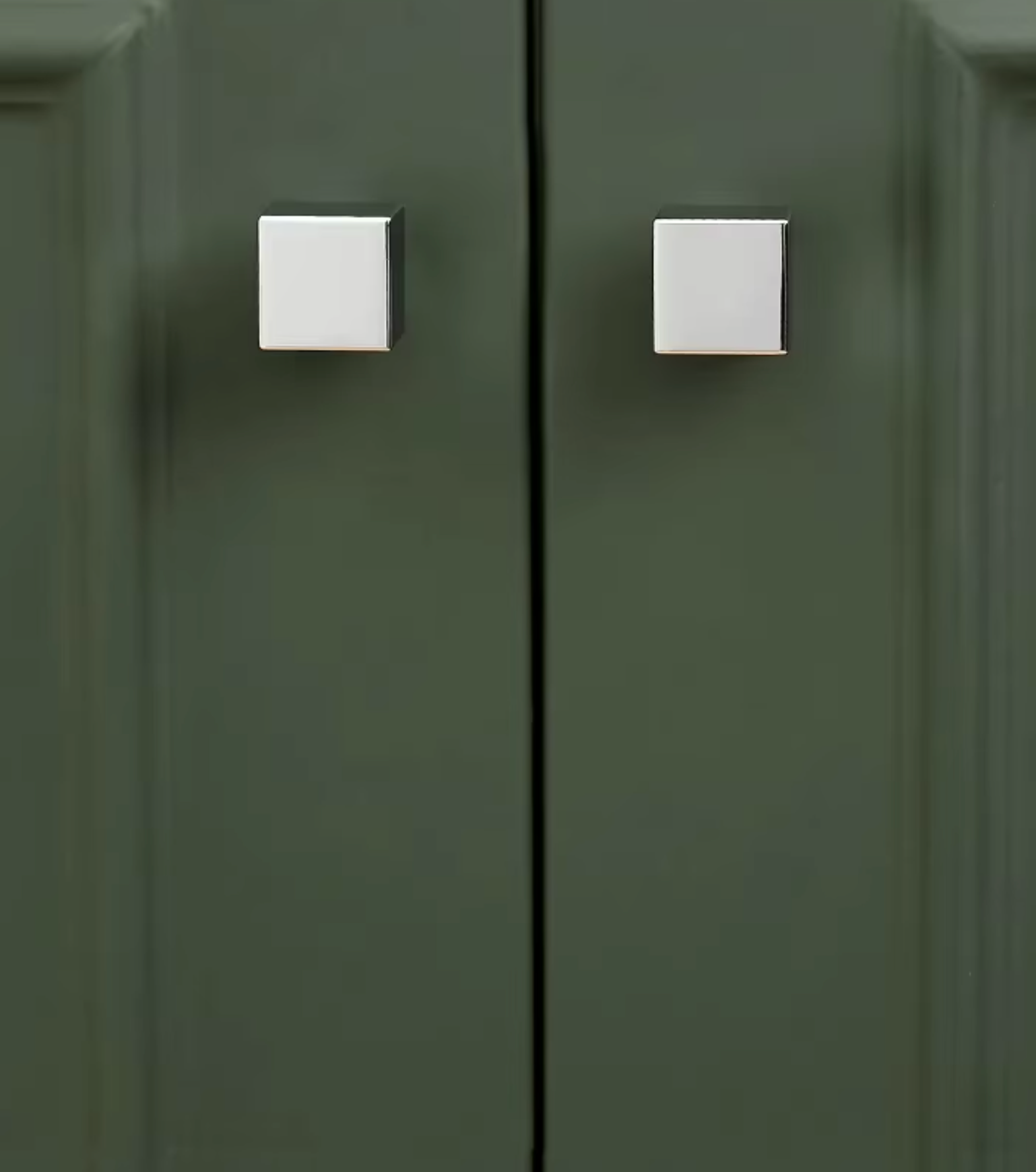A close-up of a dark olive green cabinet door with two square silver metal knobs.