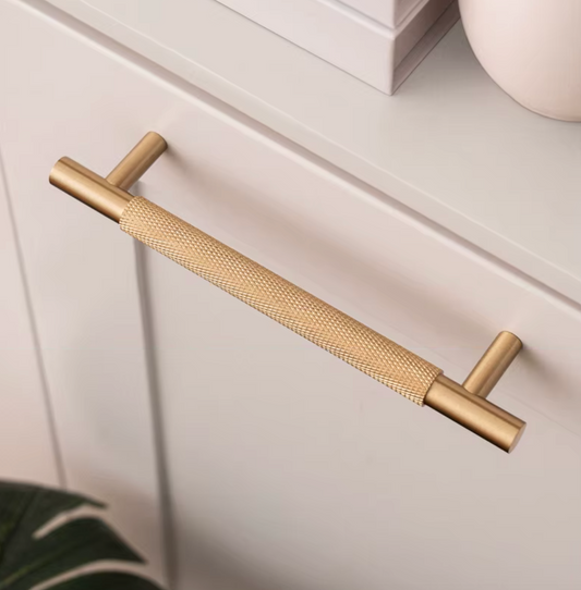 A modern two-piece cabinet pull handle in brushed gold and textured brass, mounted on a white drawer front.