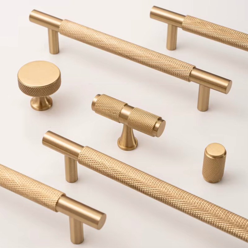 A set of brushed brass cabinet hardware, including two long bar pulls with knurled textured grips, two round knobs, and two cylindrical pulls, arranged on a clean white background.
