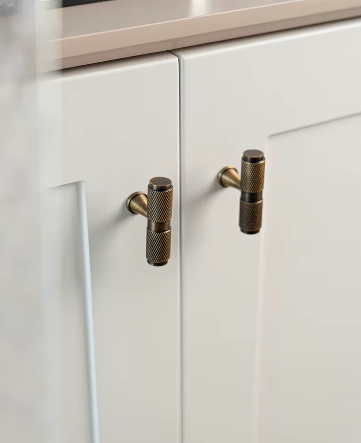 Close-up of two white cabinet doors with vertical brushed brass or bronze knobs, showing part of a light countertop above.