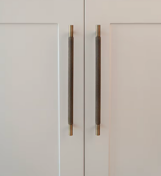 Two modern cylindrical cabinet handles with a textured dark gray center and brushed gold end caps, mounted on white paneled doors.