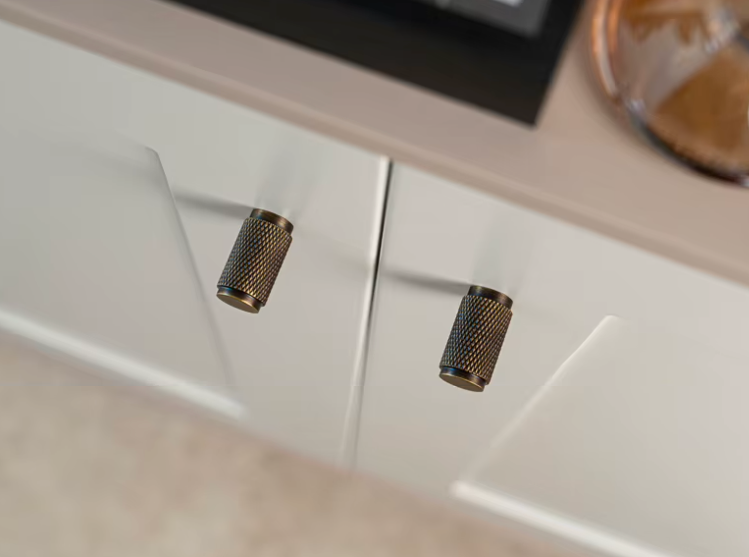 Two cylindrical brushed metal cabinet knobs with a knurled textured finish, mounted on white modern kitchen cabinets.