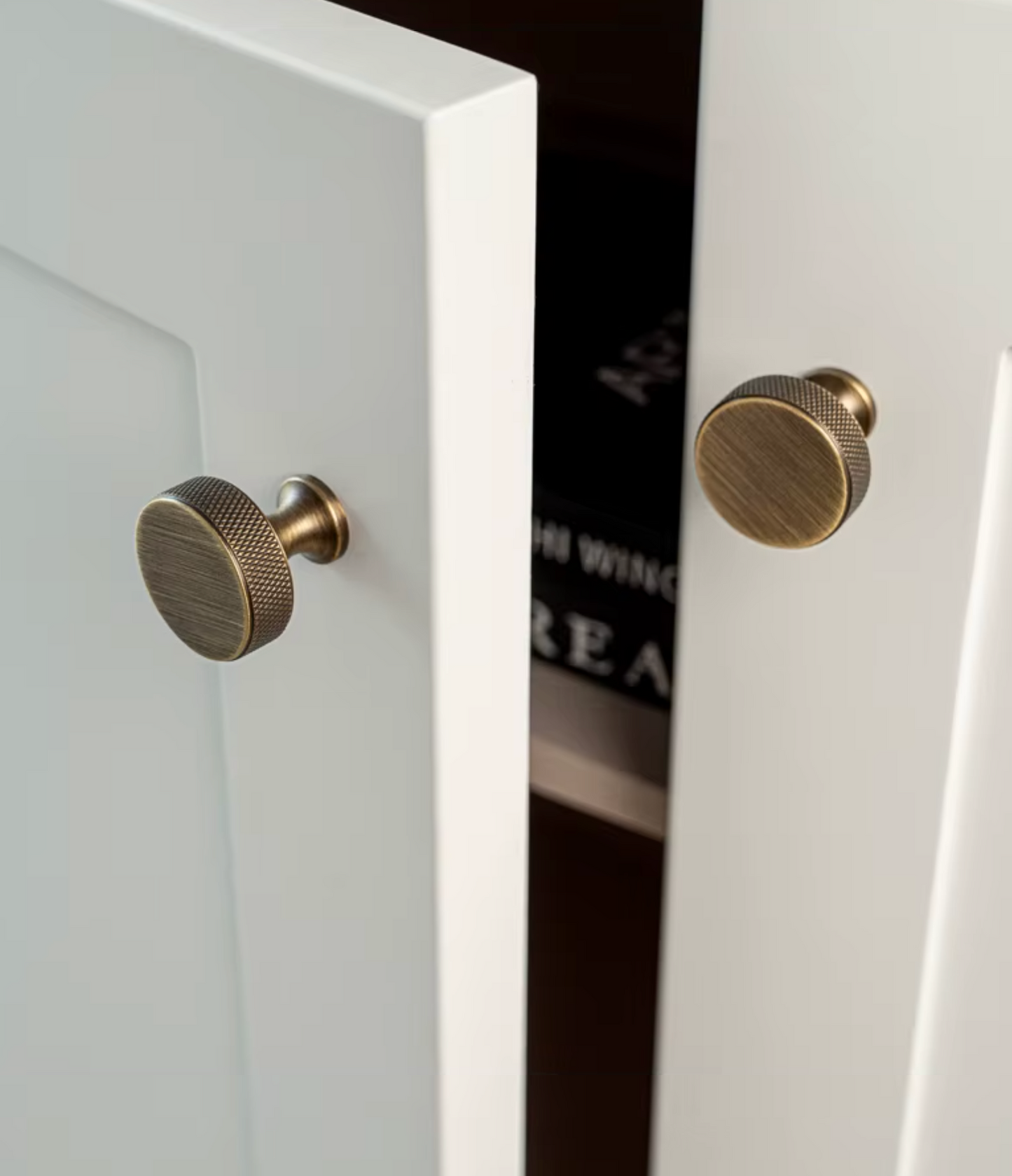Two round brass cabinet knobs with a knurled textured finish mounted on white paneled doors.