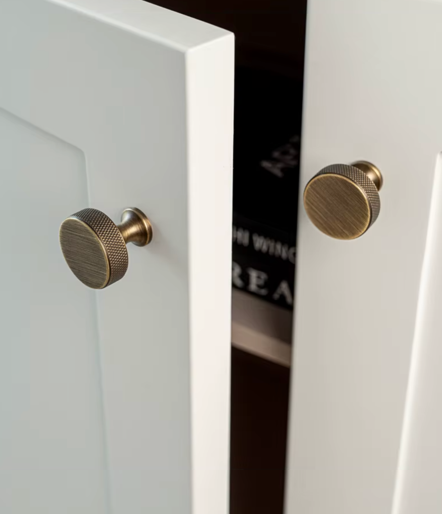 Two round brass cabinet knobs with a knurled textured finish mounted on white paneled doors.