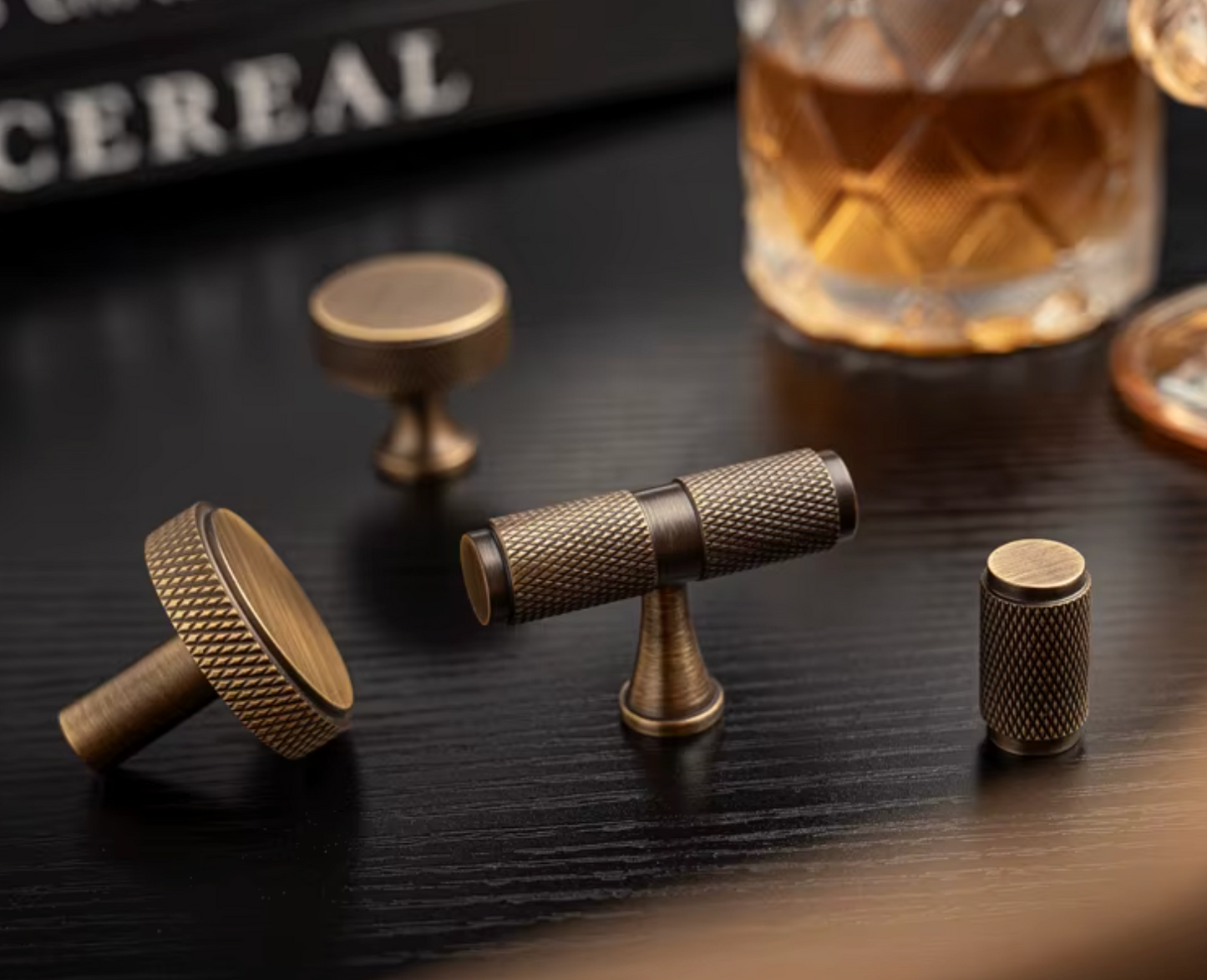 Three brass cabinet knobs with a textured, vintage finish displayed on a dark wooden tabletop .
