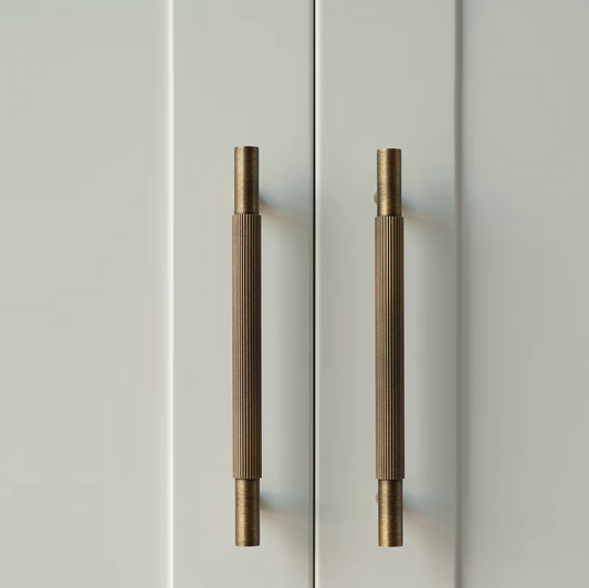 Two vertical brushed brass cabinet handles mounted on a white paneled door.