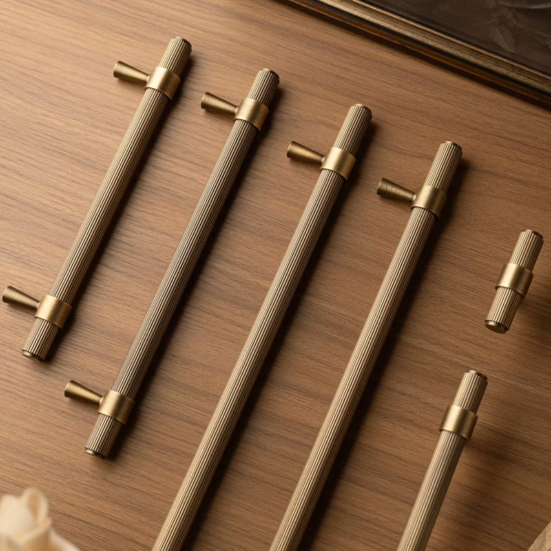 A set of modern cabinet handles with a ribbed metallic finish, shown in a warm, close-up product shot on a wooden surface.