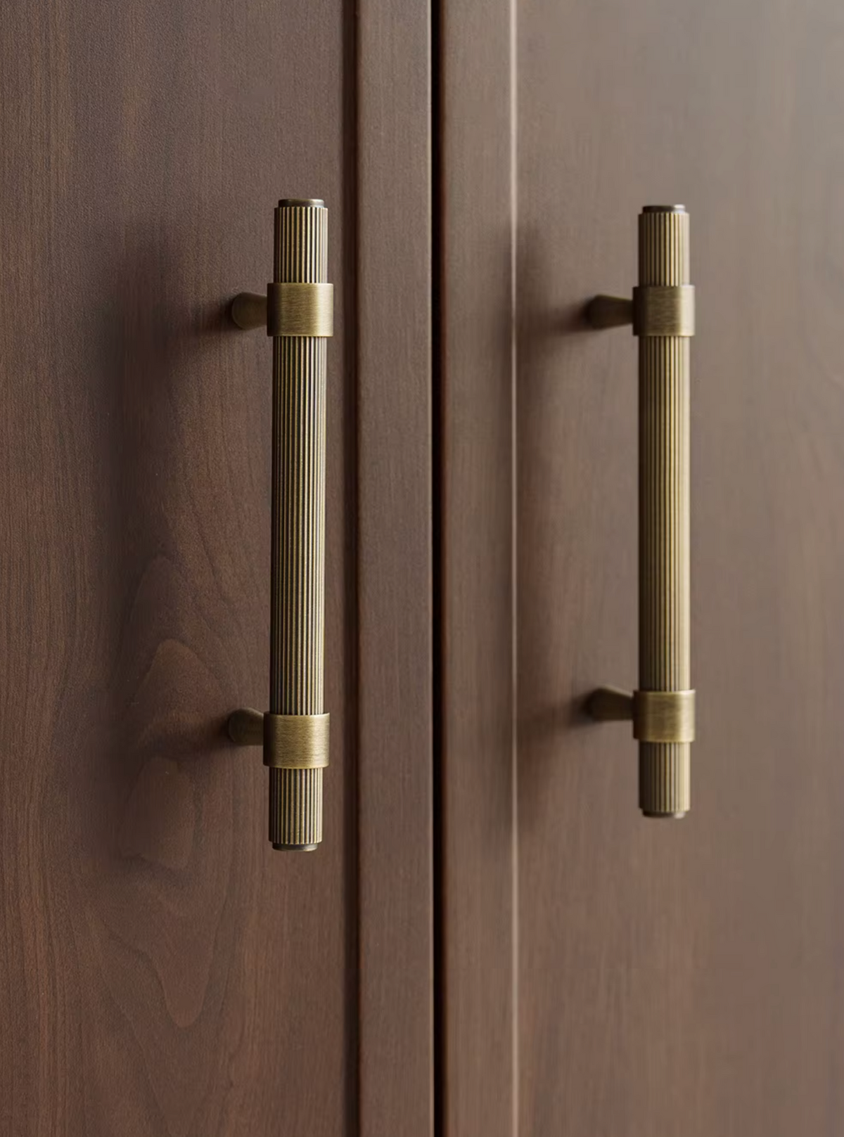 Two long, ribbed brass cabinet handles mounted on dark brown wooden doors.