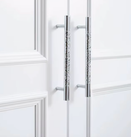 Two long vertical silver metal cabinet handles with textured center sections, mounted on white paneled doors.
