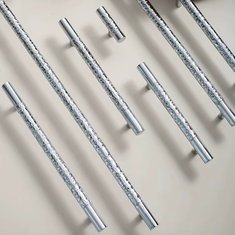 Multiple polished silver metal cabinet handles with engraved floral patterns, arranged diagonally on a light beige background.