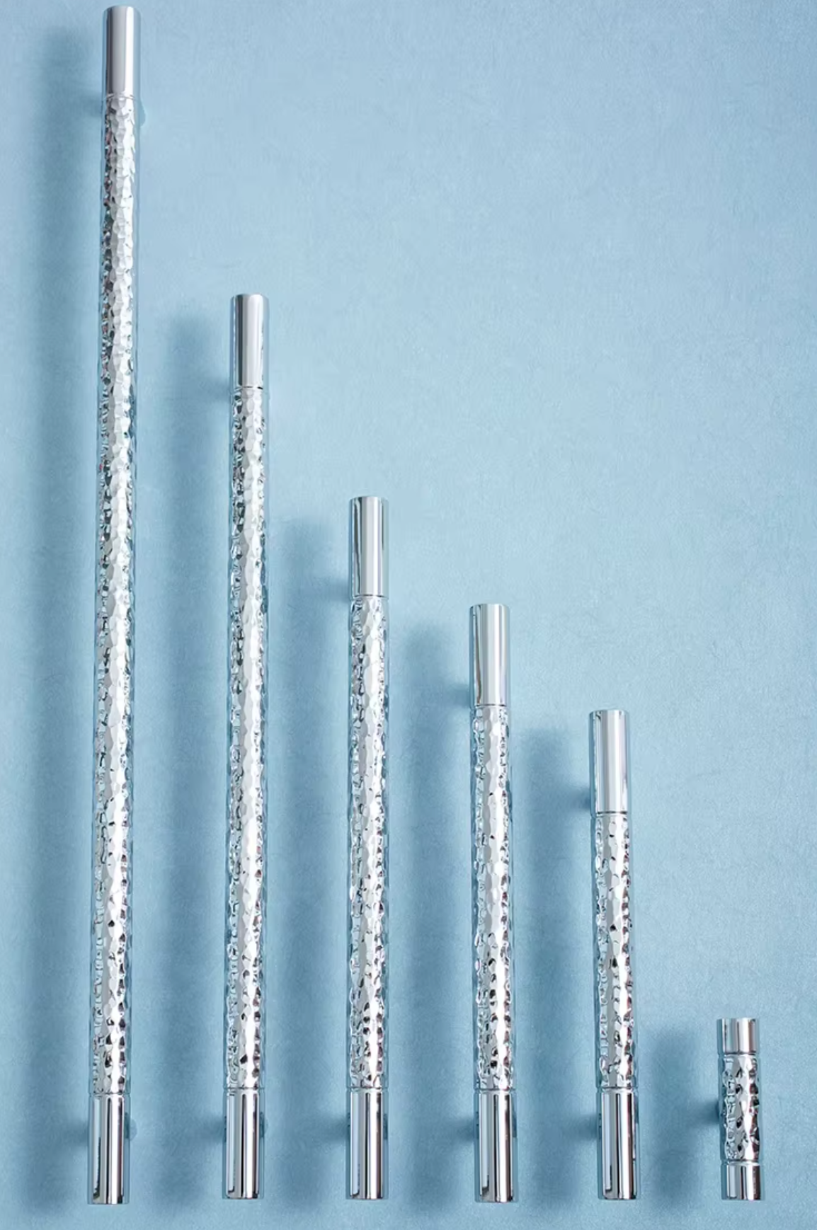 Six silver metal pole pieces with a textured, glittery pattern, arranged in descending size order against a solid light blue background.