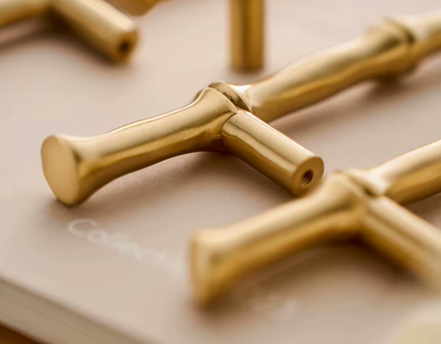 Close-up of polished brass T-shaped cabinet knobs resting on a neutral beige surface.