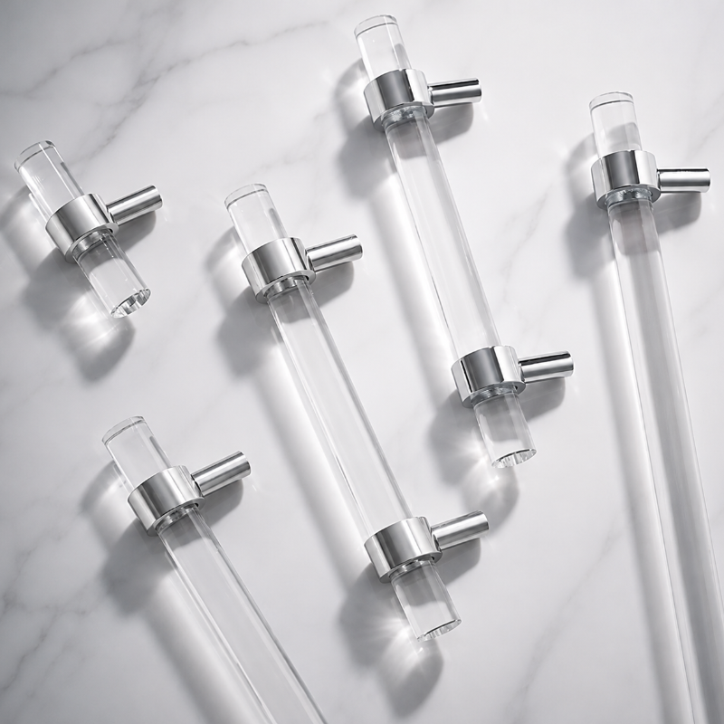 Six clear glass drawer pull handles with brushed silver metal end caps, arranged diagonally on a white marble background.