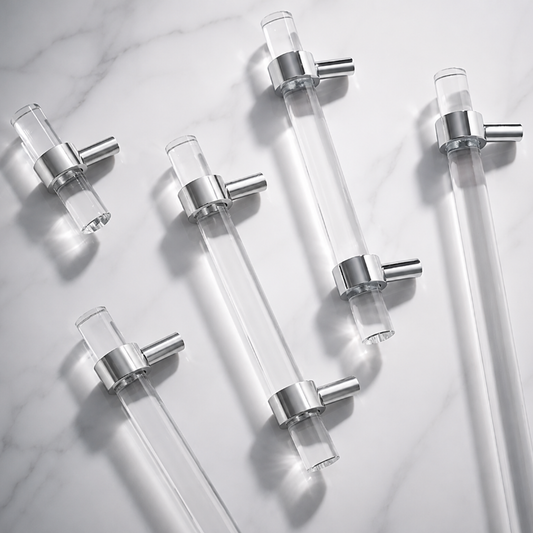 Six clear glass drawer pull handles with brushed silver metal end caps, arranged diagonally on a white marble background.
